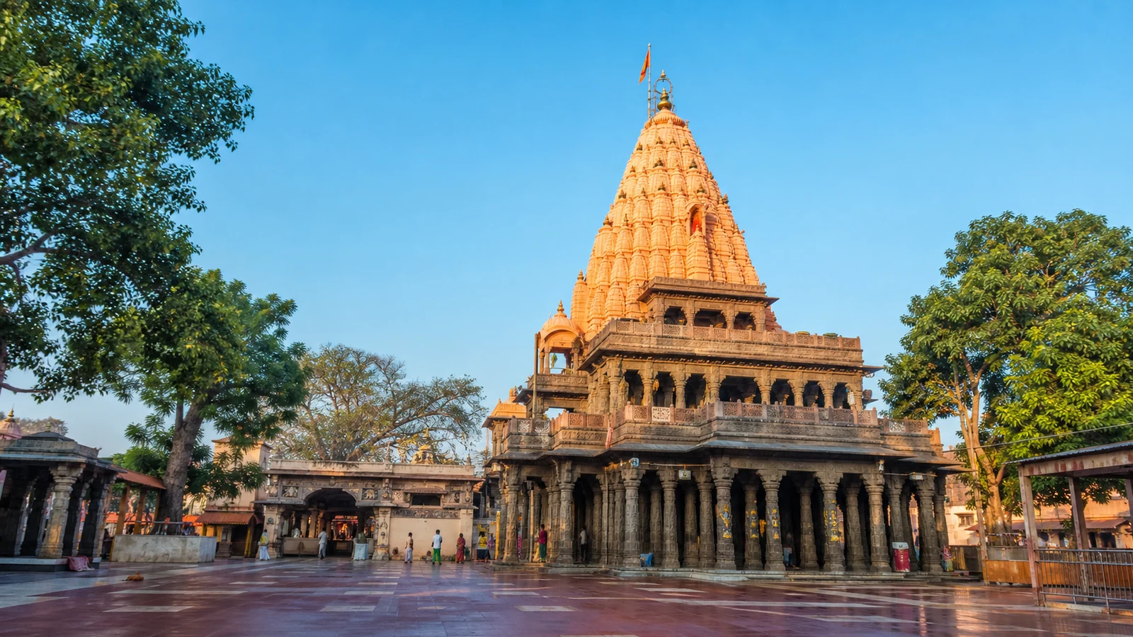 Mahakaleshwar Jyotirlinga Temple courtyard in Ujjain, with the orange shikhara rising above a dark stone pillared mandapa.